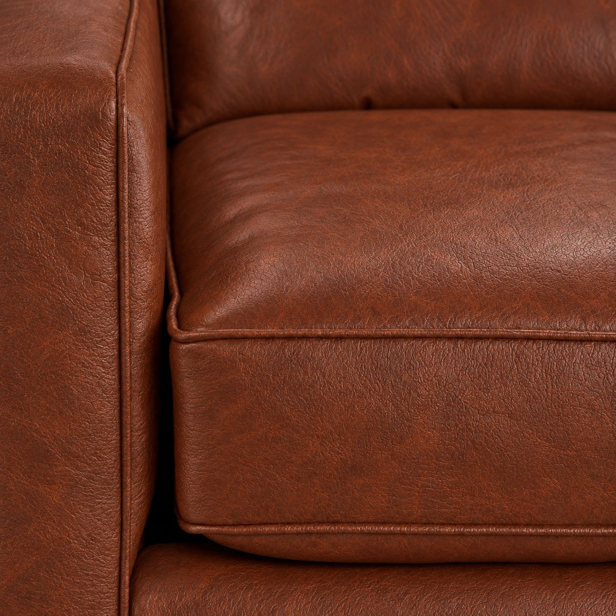 Close-up of the City Leather Chair - Brown showing the leather grain, piped seat cushion and matching upholstered arm