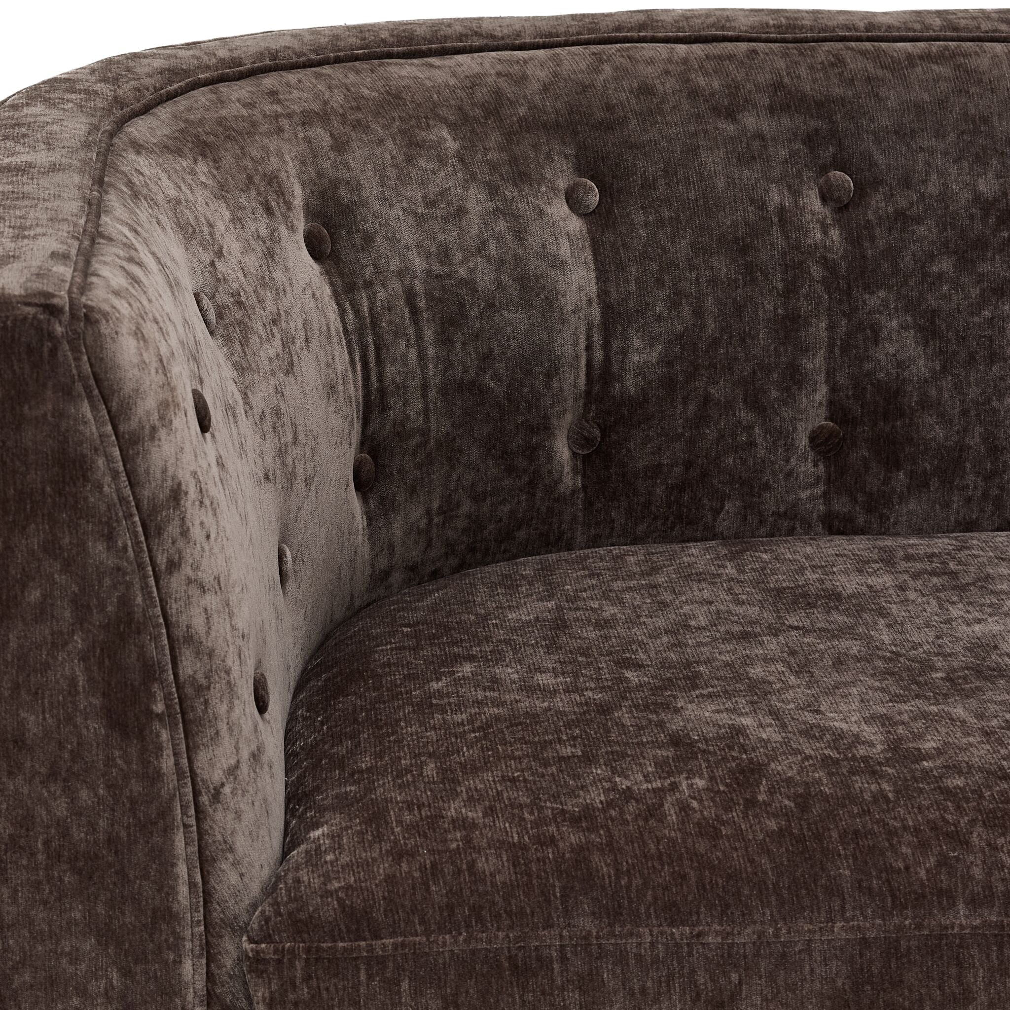 Tresor sofa close-up showing dark brown velvet-finish upholstery, curved arm and button-tufted back
