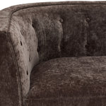 Tresor chair close-up showing dark brown velvet-finish upholstery, curved arm and button-tufted back